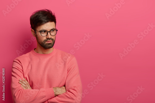 Photo of contemplative unshaven man in glasses keeps hands crossed over chest, thinks over preparing something interesting for project, ponders on how to solve situation, dressed in rosy sweater © wayhome.studio 