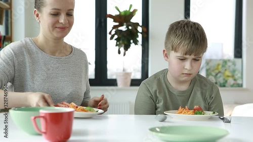 Mom feeds the baby with vegetables. Unhappy child sitting at breakfast. Boy dont want to eat   vegetables. 