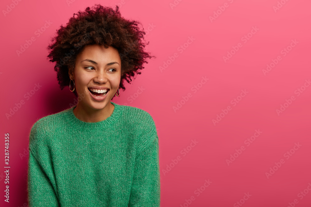 Pretty curly haired woman looks aside with dreamy happy expression, smiles broadly, expresses good emotions, wears green sweater, has appealing appearance, isolated on pink wall with empty space Pretty curly haired woman looks aside with dreamy happy expression, smiles broadly, expresses good emotions, wears green sweater, has appealing appearance, isolated on pink wall with empty space