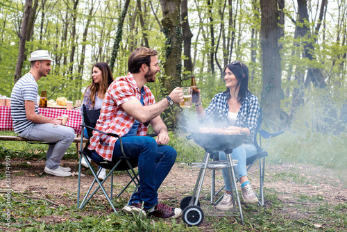 Group of friends making barbecue and having picnic in nature