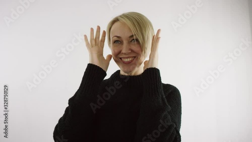 Adult middle aged caucasian blond woman is closing and opening her face with her palms against white background in bright interior