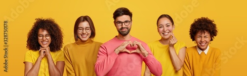 Картината върху платно Pleased bearded adult man makes heart gesture over chest, poses between four women with cheerful expressions