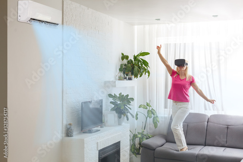 Young happy woman switching on air conditioner sitting on couch at convenient cozy home, lady relaxing on sofa in living room holding remote climate control to cooler system set comfort temperature © Angelov