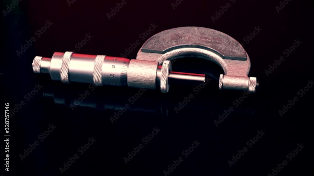 Close-up isolated measuring instrument micrometer on a black background rotates. Measuring tool. Metalworking and measurements Close-up isolated measuring instrument micrometer on a black background rotates. Measuring tool. Metalworking and measurements