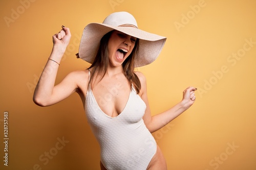 Young beautiful brunette woman on vacation wearing swimsuit and summer hat Dancing happy and cheerful, smiling moving casual and confident listening to music