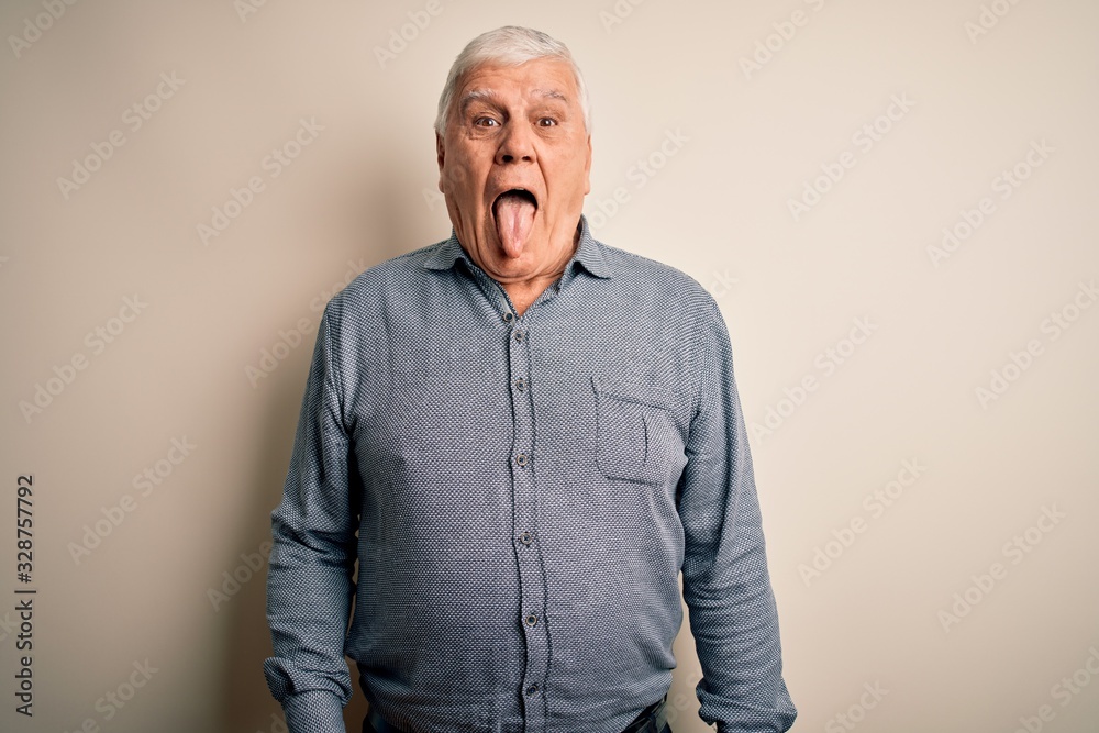 Senior handsome hoary man wearing casual shirt standing over isolated white background sticking tongue out happy with funny expression. Emotion concept.