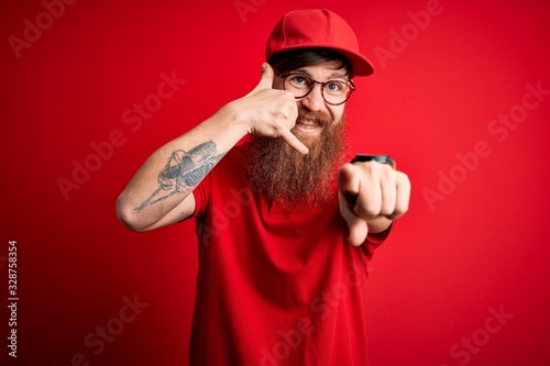 Young handsome delivery man wearing glasses and red cap over isolated background smiling doing talking on the telephone gesture and pointing to you. Call me.