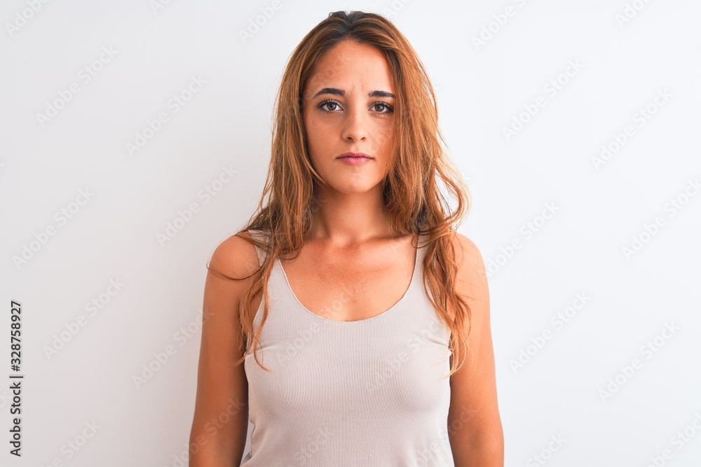 Young redhead woman wearing casual t-shirt stading over white isolated background with serious expression on face. Simple and natural looking at the camera. Young redhead woman wearing casual t-shirt stading over white isolated background with serious expression on face. Simple and natural looking at the camera.