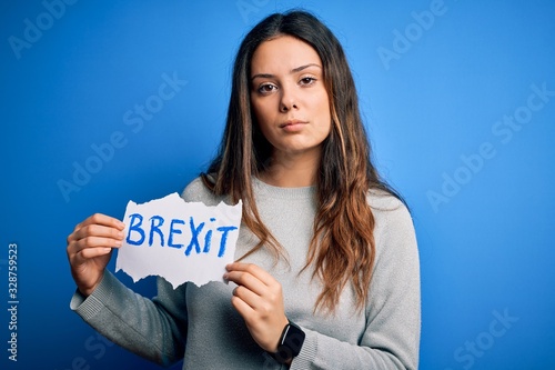 Young beautiful brunette woman holding paper with brexit message over blue background with a confident expression on smart face thinking serious