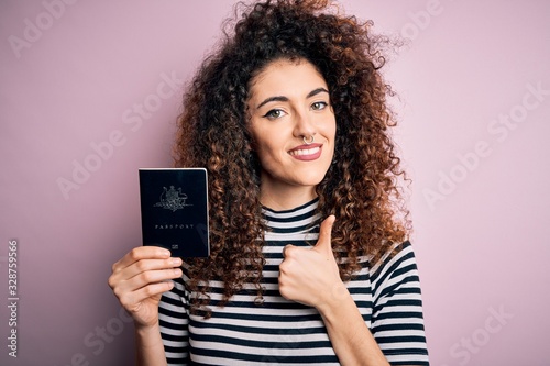 Beautiful tourist woman with curly hair and piercing holding australia australian passport id happy with big smile doing ok sign, thumb up with fingers, excellent sign