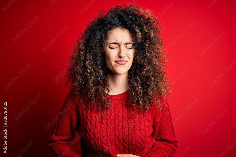Young beautiful woman with curly hair and piercing wearing casual red sweater with hand on stomach because indigestion, painful illness feeling unwell. Ache concept. Young beautiful woman with curly hair and piercing wearing casual red sweater with hand on stomach because indigestion, painful illness feeling unwell. Ache concept.