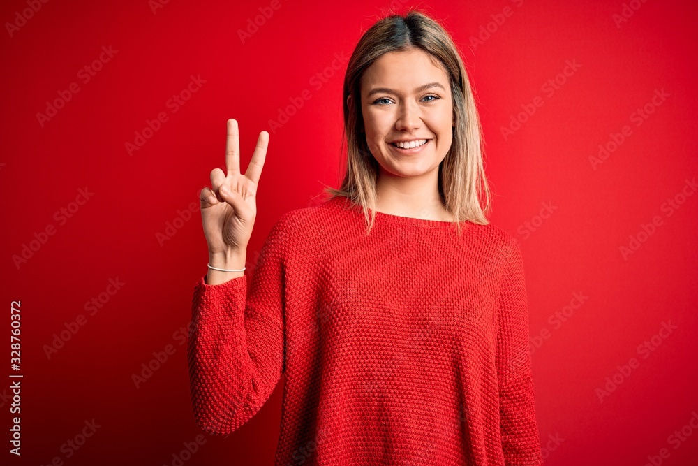Young beautiful blonde woman wearing casual sweater over red isolated background showing and pointing up with fingers number two while smiling confident and happy. Young beautiful blonde woman wearing casual sweater over red isolated background showing and pointing up with fingers number two while smiling confident and happy.