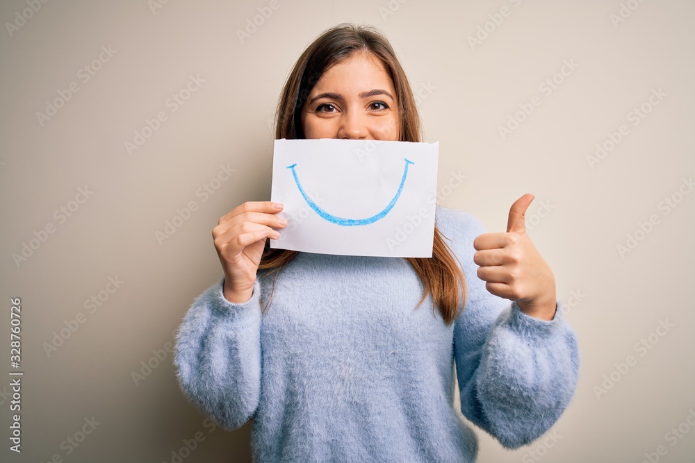 Young blonde woman holding funny smile drawing on mouth as happy expression happy with big smile doing ok sign, thumb up with fingers, excellent sign Young blonde woman holding funny smile drawing on mouth as happy expression happy with big smile doing ok sign, thumb up with fingers, excellent sign