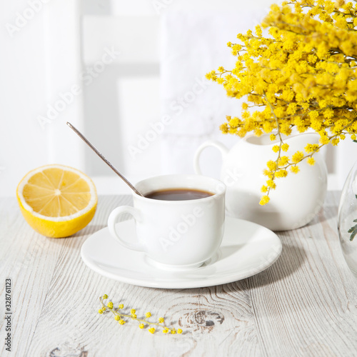 Fototapeta Naklejka Na Ścianę i Meble -  Morning coffee on table. Vase with mimosa, a symbol of Women's Day, a jug of water on a sunny day.