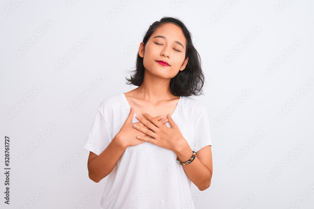 Young chinese woman wearing casual t-shirt standing over isolated white background smiling with hands on chest with closed eyes and grateful gesture on face. Health concept. Young chinese woman wearing casual t-shirt standing over isolated white background smiling with hands on chest with closed eyes and grateful gesture on face. Health concept.
