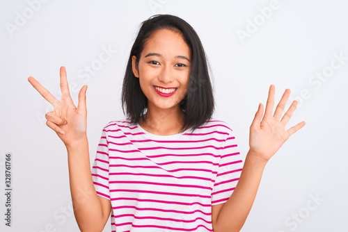 Young chinese woman wearing striped t-shirt standing over isolated white background showing and pointing up with fingers number eight while smiling confident and happy.