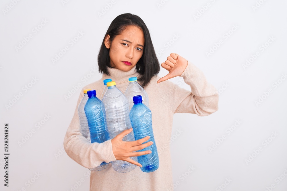 Young beautiful chinese woman recycling plastic bottles over isolated white background with angry face, negative sign showing dislike with thumbs down, rejection concept Young beautiful chinese woman recycling plastic bottles over isolated white background with angry face, negative sign showing dislike with thumbs down, rejection concept