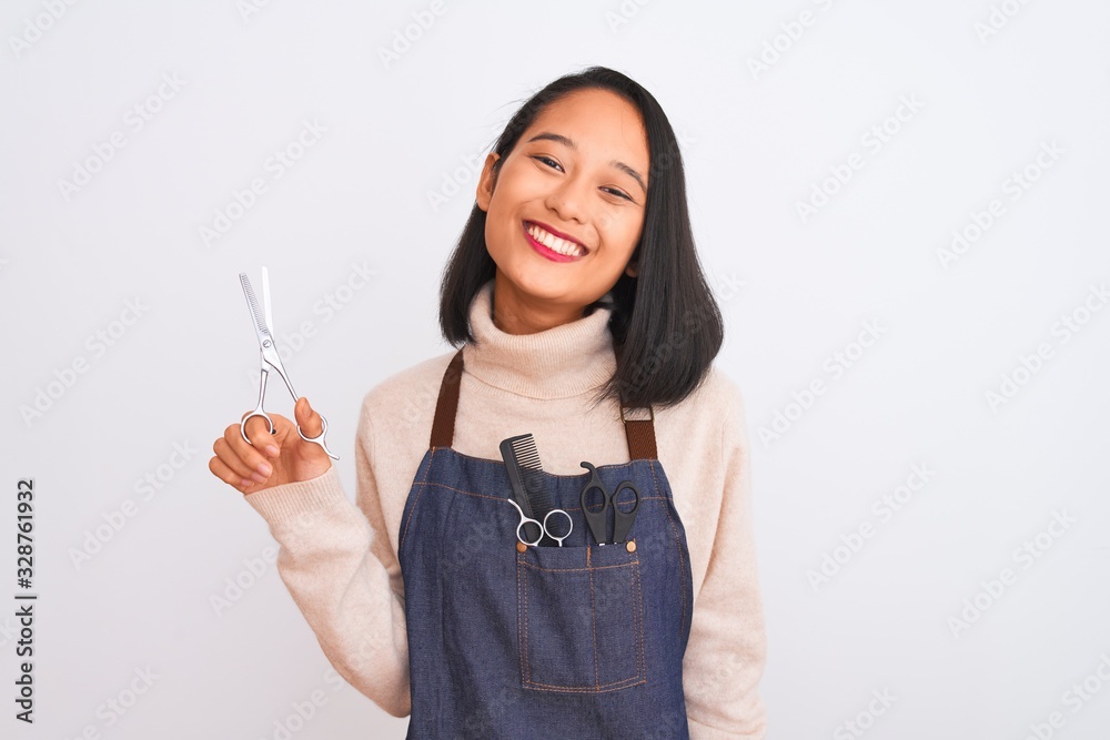 Chinese hairdresser woman wearing apron holding scissors over isolated white background with a happy face standing and smiling with a confident smile showing teeth