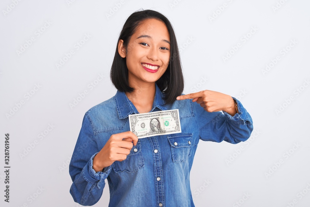 Young beautiful chinese woman holding one dollar standing over isolated white background with surprise face pointing finger to himself Young beautiful chinese woman holding one dollar standing over isolated white background with surprise face pointing finger to himself