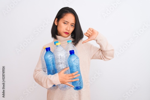 Young beautiful chinese woman recycling plastic bottles over isolated white background with angry face, negative sign showing dislike with thumbs down, rejection concept