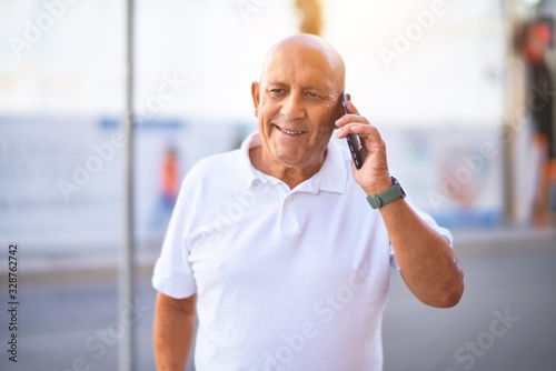Senior handsome man smiling happy and confident. Standing with smile on face talking by the phone at town street