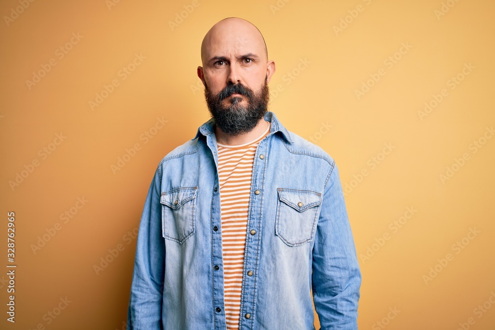 Handsome bald man with beard wearing casual denim jacket and striped t-shirt Relaxed with serious expression on face. Simple and natural looking at the camera. Handsome bald man with beard wearing casual denim jacket and striped t-shirt Relaxed with serious expression on face. Simple and natural looking at the camera.