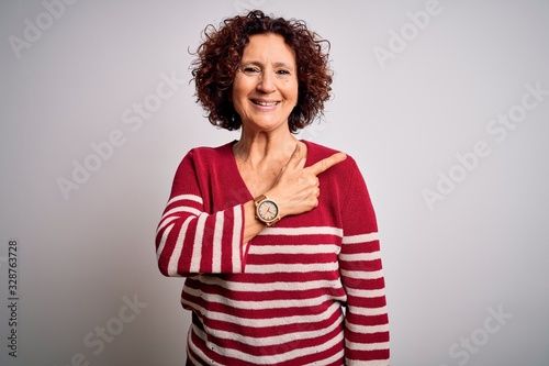 Middle age beautiful curly hair woman wearing casual striped sweater over white background cheerful with a smile of face pointing with hand and finger up to the side with happy and natural expression