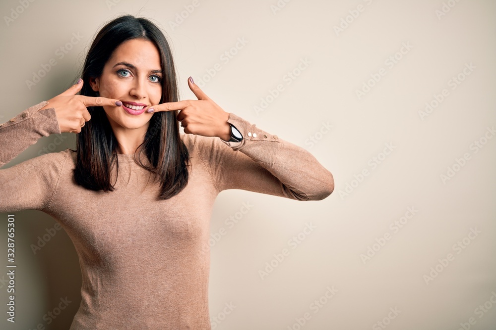 Obraz premium Young brunette woman with blue eyes wearing casual sweater over isolated white background smiling cheerful showing and pointing with fingers teeth and mouth. Dental health concept.