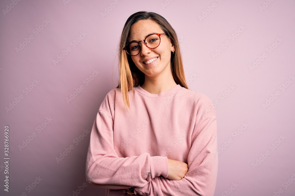 Beautiful blonde woman with blue eyes wearing sweater and glasses over pink background happy face smiling with crossed arms looking at the camera. Positive person. Beautiful blonde woman with blue eyes wearing sweater and glasses over pink background happy face smiling with crossed arms looking at the camera. Positive person.