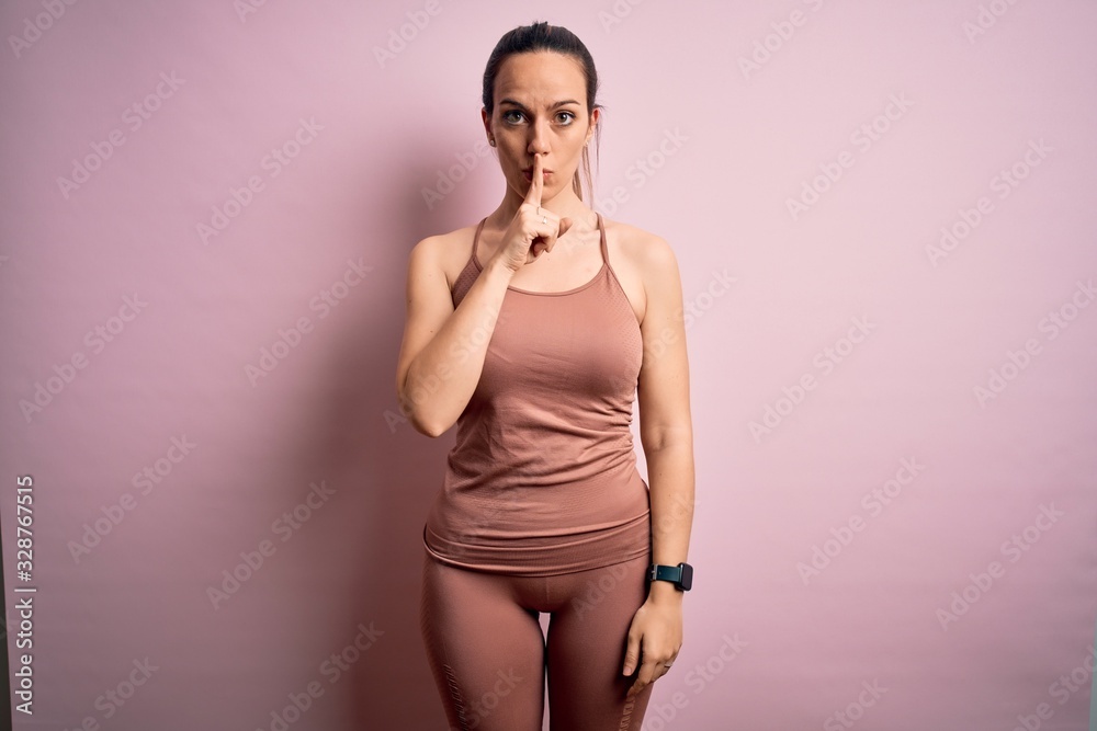 Young blonde fitness woman wearing sport workout clothes over pink isolated background asking to be quiet with finger on lips. Silence and secret concept. Young blonde fitness woman wearing sport workout clothes over pink isolated background asking to be quiet with finger on lips. Silence and secret concept.