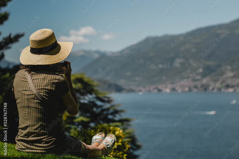 Healthy woman celebrating during a beautiful sunset. Happy and Free. Young woman sits at lake, at seaside looking at mountains and taking shots of picturesque view. 