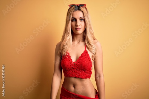 Young beautiful blonde woman on vacation wearing bikini over isolated yellow background looking sleepy and tired, exhausted for fatigue and hangover, lazy eyes in the morning.