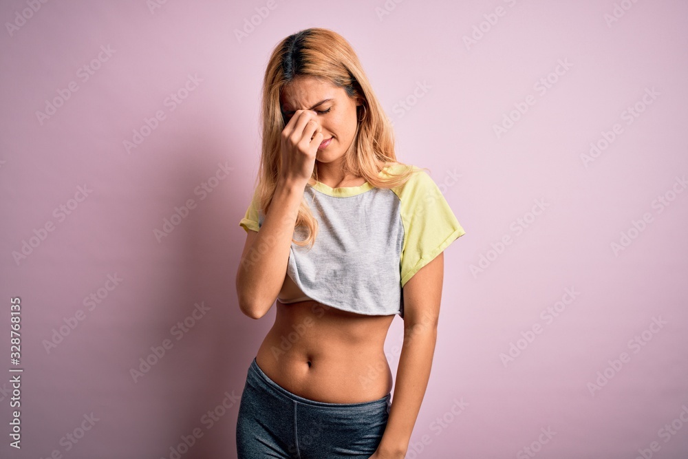 Young beautiful blonde sportswoman doing sport wearing sportswear over pink background tired rubbing nose and eyes feeling fatigue and headache. Stress and frustration concept. Young beautiful blonde sportswoman doing sport wearing sportswear over pink background tired rubbing nose and eyes feeling fatigue and headache. Stress and frustration concept.