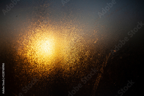 Cloudy glass in warm and cold colors. Dawn behind a blurry transparent surface. Abstract warm background. The texture of the glass is condensed. The soft light of the morning sun on a rough surface.