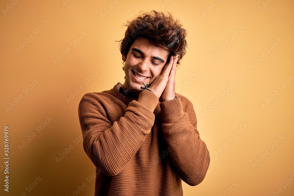 Young handsome man wearing casual shirt and sweater over isolated yellow background sleeping tired dreaming and posing with hands together while smiling with closed eyes. Young handsome man wearing casual shirt and sweater over isolated yellow background sleeping tired dreaming and posing with hands together while smiling with closed eyes.