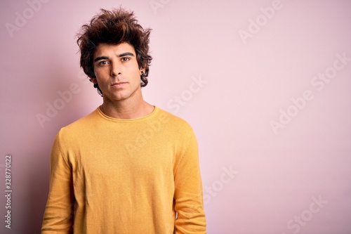 Young handsome man wearing yellow casual t-shirt standing over isolated pink background Relaxed with serious expression on face. Simple and natural looking at the camera.