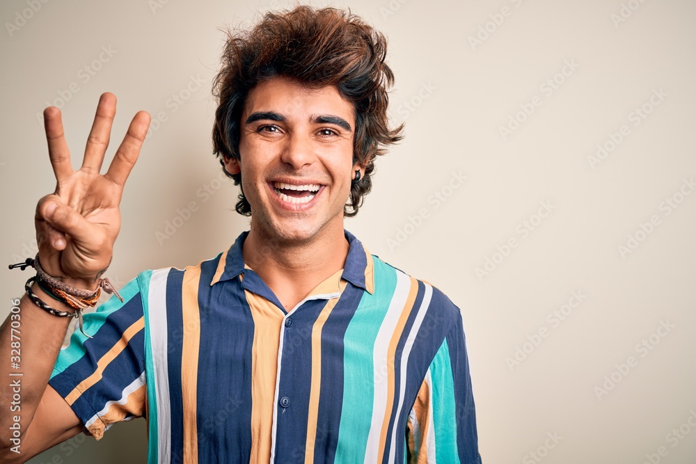 Young man on vacation wearing summer colorful shirt standing over isolated white background showing and pointing up with fingers number three while smiling confident and happy.