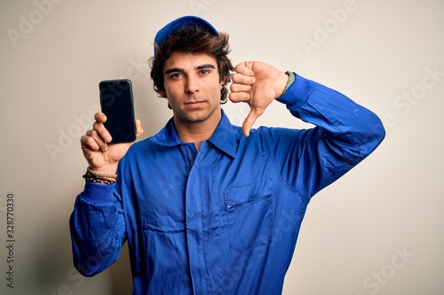 Konstfotografi Young mechanic man wearing uniform holding smartphone over isolated white backgr