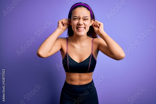 Young beautiful sporty girl doing sport wearing sportswear over isolated purple background Smiling pulling ears with fingers, funny gesture. Audition problem © Krakenimages.com