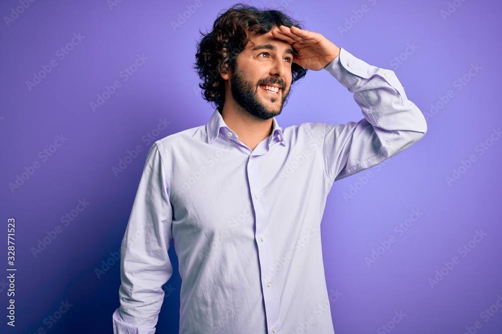 Young handsome business man with beard wearing shirt standing over purple background very happy and smiling looking far away with hand over head. Searching concept.