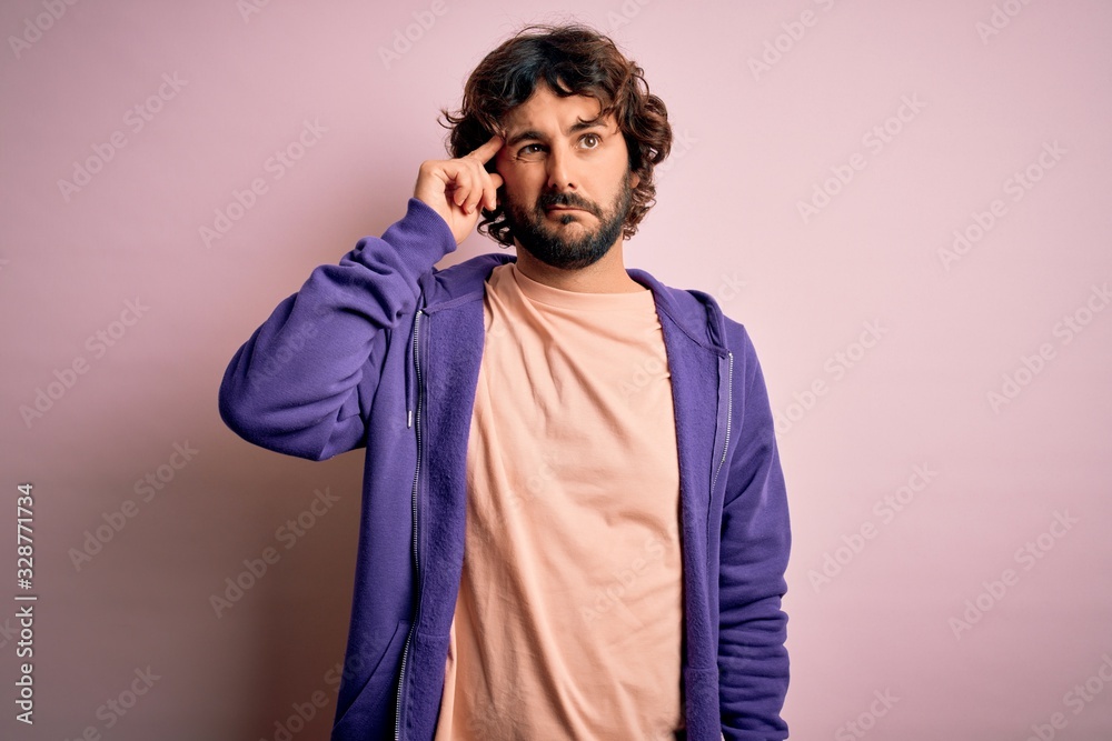 Young handsome sporty man with beard wearing casual sweatshirt over pink background worried and stressed about a problem with hand on forehead, nervous and anxious for crisis