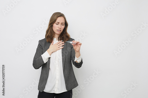 Businesswoman holding a thermometer looking concerned and placing her hand on her breast afraid of having the influenza and disease corona virus covid-19