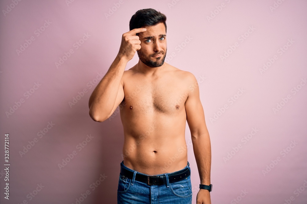 Young handsome strong man with beard shirtless standing over isolated pink background pointing unhappy to pimple on forehead, ugly infection of blackhead. Acne and skin problem
