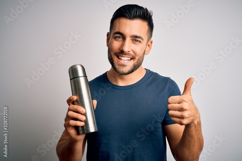 Young handsome tourist man drinking thermo with water over isolated white background happy with big smile doing ok sign, thumb up with fingers, excellent sign