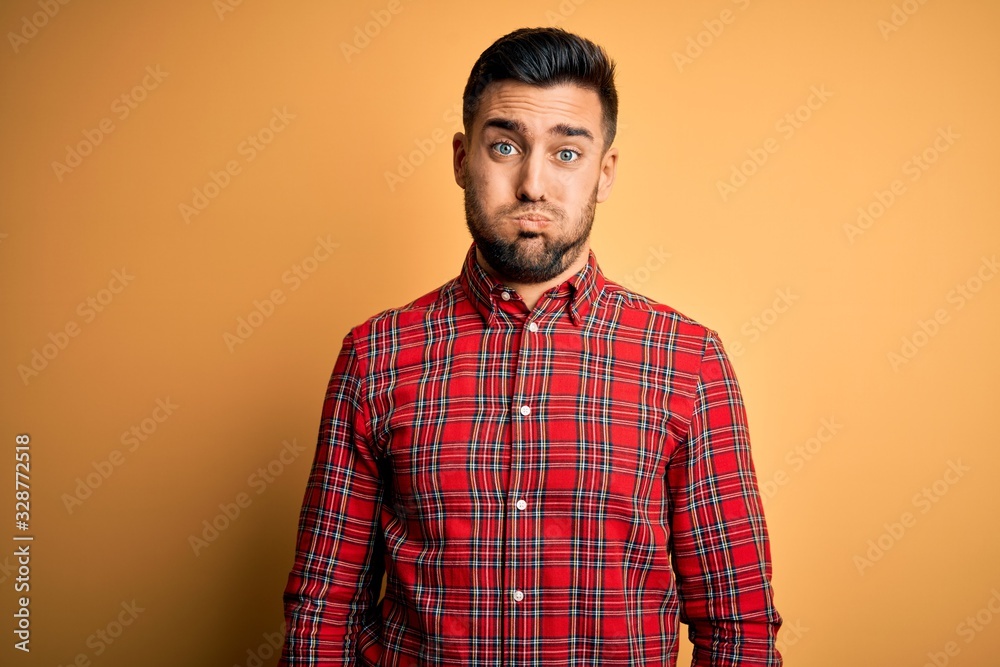Obraz premium Young handsome man wearing casual shirt standing over isolated yellow background puffing cheeks with funny face. Mouth inflated with air, crazy expression.