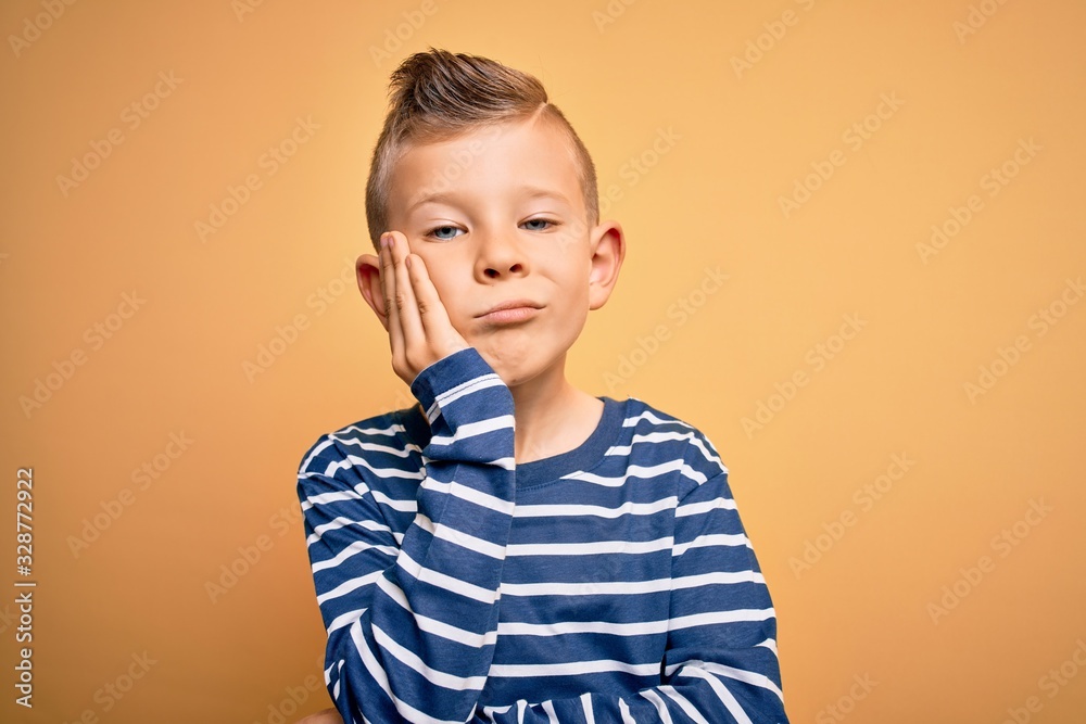 Young little caucasian kid with blue eyes wearing nautical striped shirt over yellow background thinking looking tired and bored with depression problems with crossed arms. Young little caucasian kid with blue eyes wearing nautical striped shirt over yellow background thinking looking tired and bored with depression problems with crossed arms.