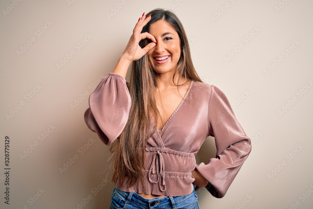 Young beautiful brunette elegant woman with long hair standing over isolated background doing ok gesture with hand smiling, eye looking through fingers with happy face. Young beautiful brunette elegant woman with long hair standing over isolated background doing ok gesture with hand smiling, eye looking through fingers with happy face.