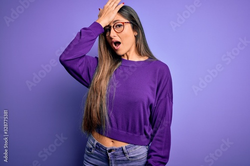 Young beautiful smart woman wearing glasses over purple isolated background surprised with hand on head for mistake, remember error. Forgot, bad memory concept.