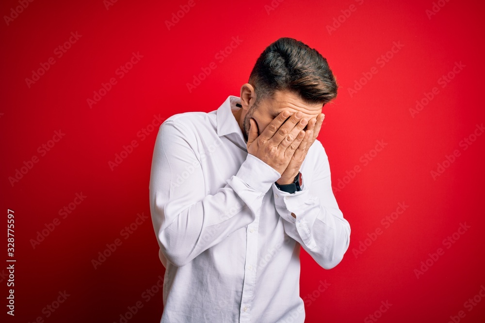 Young business man with blue eyes wearing elegant shirt standing over red isolated background with sad expression covering face with hands while crying. Depression concept. Young business man with blue eyes wearing elegant shirt standing over red isolated background with sad expression covering face with hands while crying. Depression concept.