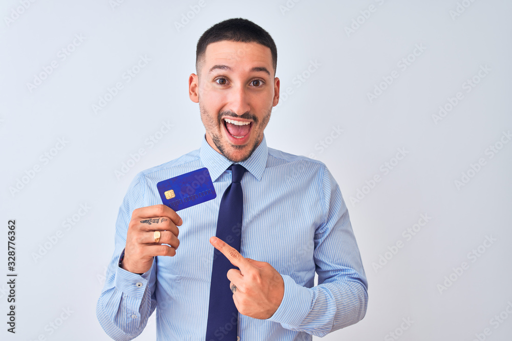 Young business man holding credit card over isolated background very happy pointing with hand and finger Young business man holding credit card over isolated background very happy pointing with hand and finger